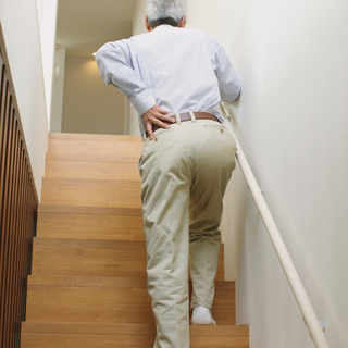 Older adult holding lower back while climbing stairs—stiff joints and limited range of motion.