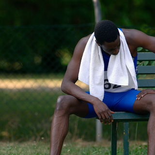 Tired runner resting on a bench with towel—next-day muscle soreness slowing recovery.
