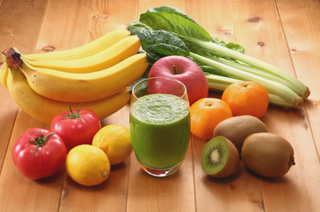 Fresh fruits and vegetables including bananas, apple, oranges, kiwi, lemons, tomatoes, and leafy greens with a glass of green smoothie on a wooden table — rich in vitamins, antioxidants, and natural energy.