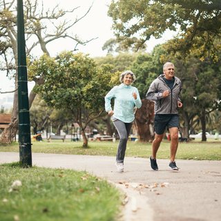 Older couple jogging outdoors in a park, representing sustained energy, mobility, and workout longevity.
