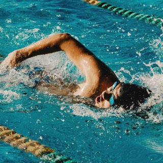 Person swimming freestyle in a pool, highlighting strength, muscle growth, and full-body power.