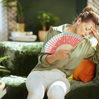 Woman fanning herself on couch — natural menopause supplement for hot flash and night sweat relief.