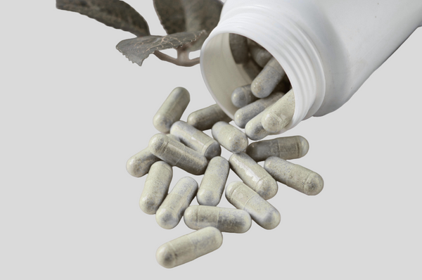 Generic white bottle of capsules spilled out on a surface, showing lower-quality supplement presentation.