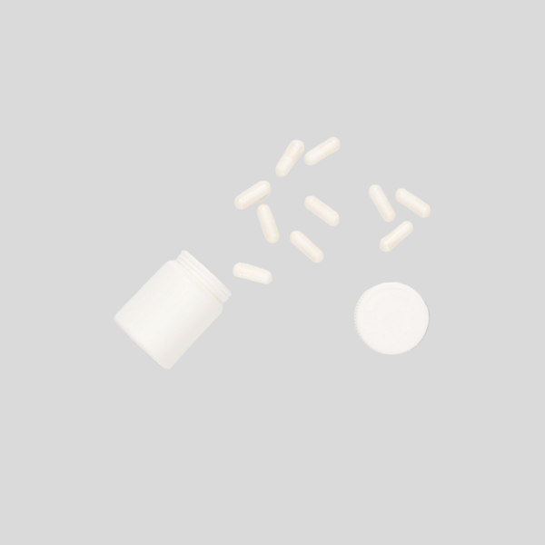 Open supplement bottle with scattered white capsules on a gray background.